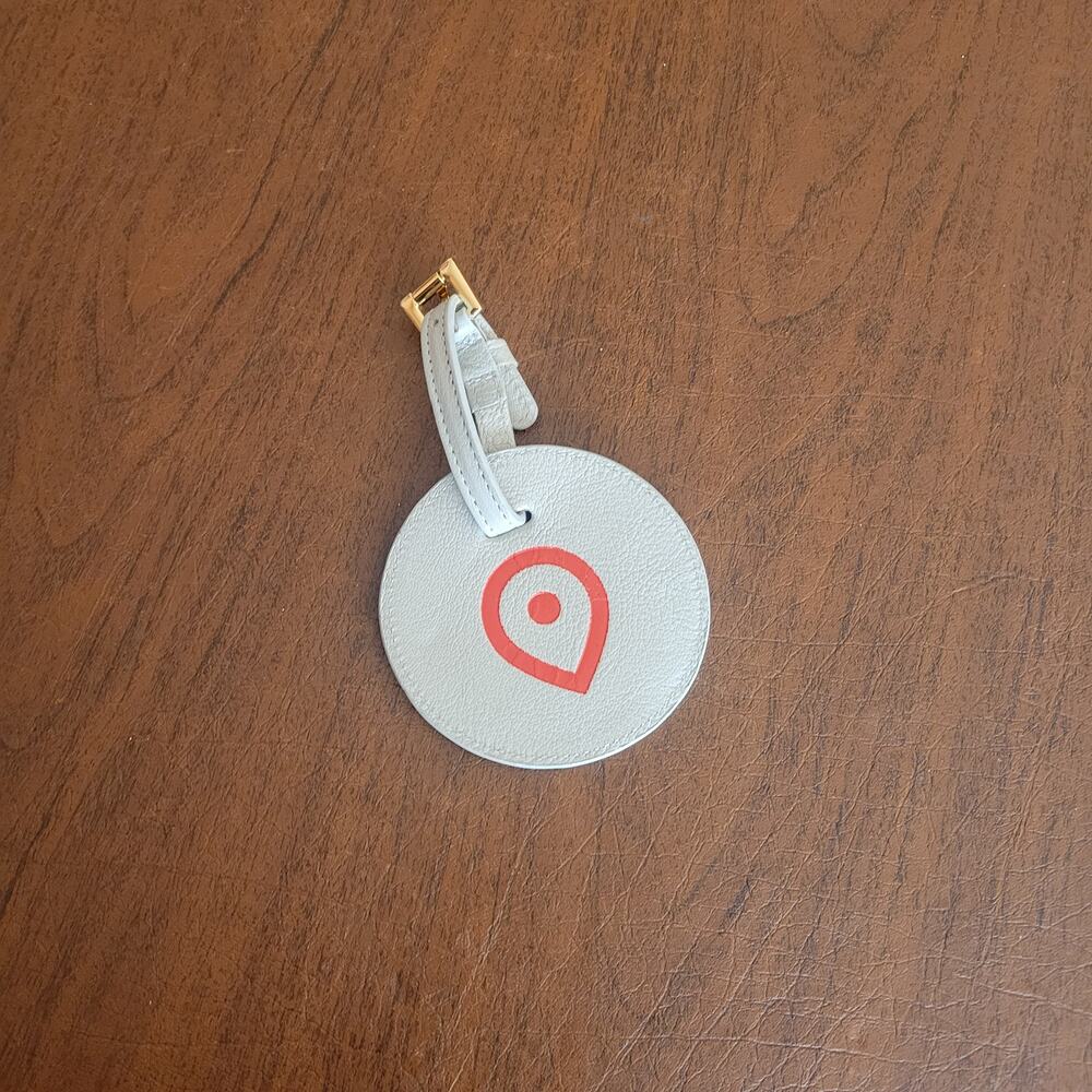 Round textured leather luggage tag in light grey with a red map